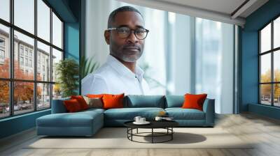 Man of African American descent, wearing glasses, stands in front of a window. He appears calm and focused, looking  at the camera. Business success concept Wall mural