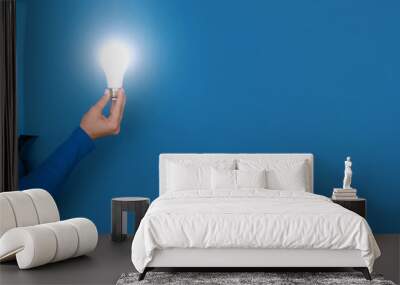 hand holding light bulb over blue background, panoramic layout Wall mural