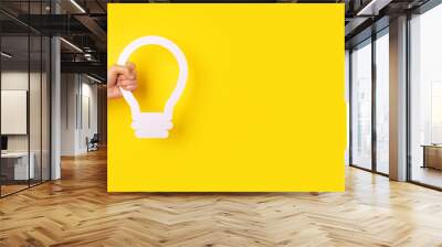 hand holding light bulb symbol over yellow background, panoramic layout image with space for text Wall mural