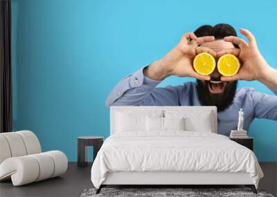 smiling hipster man holding lemon slices in front of eyes, over blue background, panoramic mock-up with space for text Wall mural