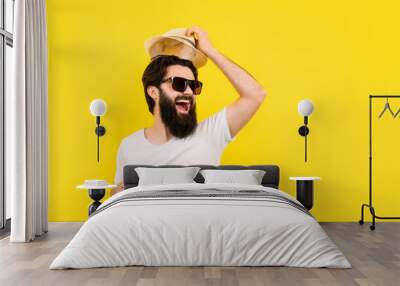 studio portrait of a cheerful bearded guy in a great mood, man in sunglasses, welcome gesture of raising the hat, concept summer vacation Wall mural