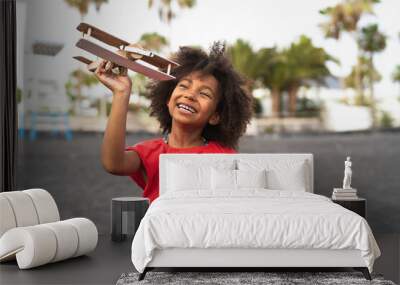 Afro child playing with wood toy airplane on the beach - Little kid having fun during summer holidays - Childhood and travel vacation concept Wall mural