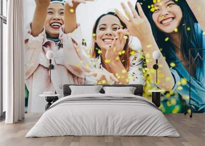 Happy Asian friends having fun throwing confetti outdoor - Young trendy people celebrating at festival event outside - Party, entertainment and youth holidays lifestyle concept Wall mural