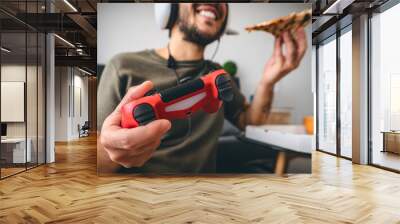 Happy man playing online video games while eating pizza fast food - Young gamer having fun on new technology console - Gaming entertainment and youth millennial generation lifestyle concept Wall mural