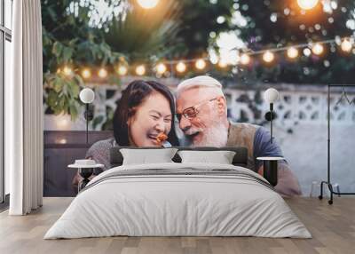 Happy senior couple having fun at dinner house party - Older people with different ethnicity doing a romantic date for celebrating anniversary - Elderly, food, drink and love concept Wall mural