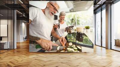 Happy senior couple having fun cooking together at home - Elderly people preparing health lunch in modern kitchen - Retired lifestyle family time and food nutrition concept Wall mural