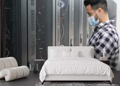 Informatic engineer working inside server room database while wearing face mask during corona virus outbreak Wall mural