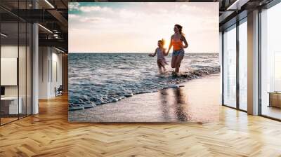 Mother and daughter running along the seashore at sunset - Happy family having fun playing together in vacation on the beach - Parenthood, happiness and love concept Wall mural