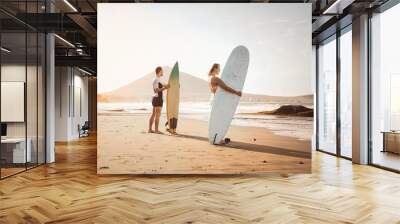 Surfers couple standing on the beach with surfboards preparing to surf on high waves - Young people having fun during surfing day - Extreme health sport and youth lifestyle culture concept Wall mural