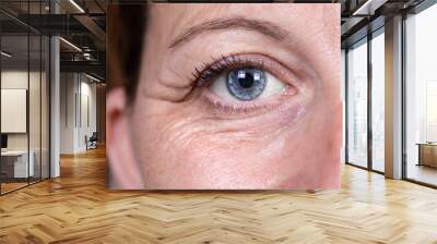 A closeup and front view on the eye area of a lady in her 40s. Heavy crow's feet, also known as laughter lines, are seen around the eye. Skin fatigue. Wall mural