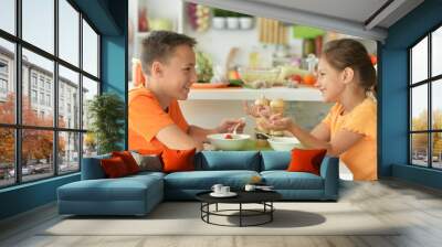 Cute brother and sister tasting salad together in kitchen Wall mural