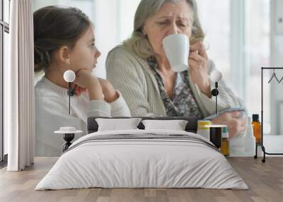 Cute girl giving medicine to sick senior woman Wall mural