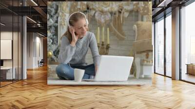 cute girl  in headphones  using laptop while sitting on  floor at home on Christmas Wall mural