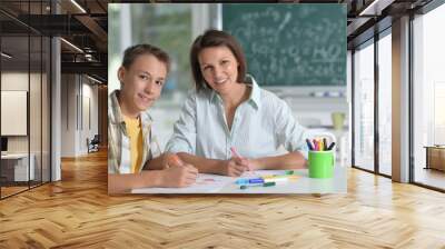 Portrait of schoolboy and teacher sitting at classroom Wall mural