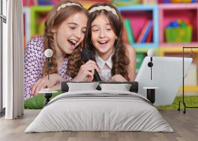 Portrait of two cute little girls singing karaoke with laptop Wall mural