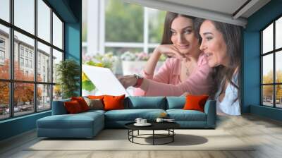 Two beautiful woman using laptop at home Wall mural