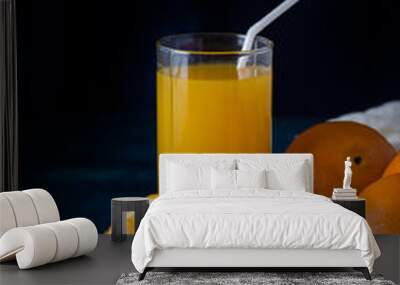 A glass of Fresh Orange Juice with a Tube, Orange slices, Oranges, white Cloth on a Dark Blue Background Wall mural