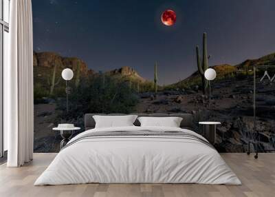 A wide-angle shot of the Blood Moon casting a reddish glow over a desert landscape, with cacti and rocks.Bloody moon.Blood moon.Full red moon. Wall mural