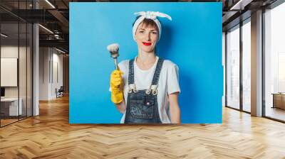 A young girl holding a brush with paint on a blue background. Painting concept, repair, building Wall mural