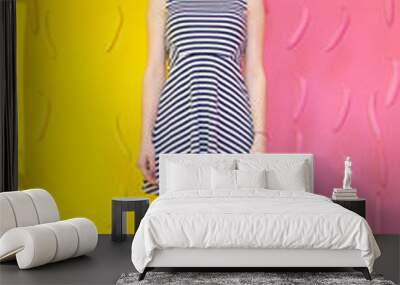 beautiful girl standing and smiling against a background of 2 colors dividing background in half a pink and yellow, saturated and weaving in the air painted bananas. Striped dress and evening shoes. Wall mural