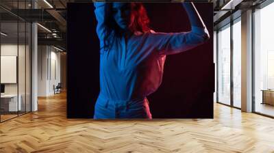 Beautiful young girl in a white shirt poses in blue and red light. On a black background studio photo Wall mural