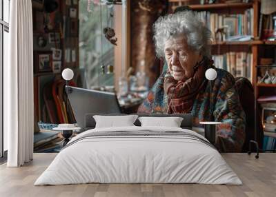 Elderly woman working on laptop at home sitting at the table. Wall mural