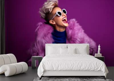 Fashionable young woman in pink fur coat and sunglasses on purple background Wall mural