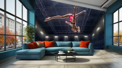 Female athlete doing a complicated exciting jump trick in a professional gym. Girl perform stunt in bright sports clothes Wall mural