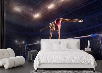 Female athlete doing a complicated exciting trick on horizontal gymnastics bars in a professional gym. Girl perform stunt in bright sports clothes Wall mural