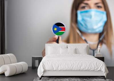 female doctor in a medical mask holds a stethoscope on a light background. Added flag of Sudan. Concept medicine, level of medicine, virus, epidemic Wall mural