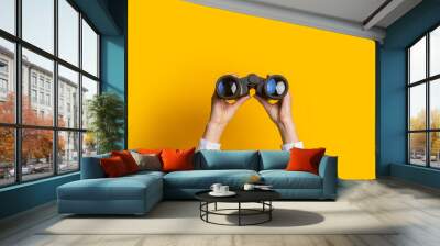 female hands hold black binoculars on a bright yellow background Wall mural