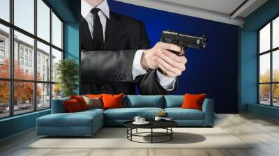 Firearms and security topic: a man in a black suit holding a gun on a dark blue background in studio isolated Wall mural