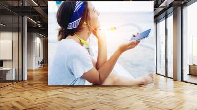 Beautiful woman using mobile phone with wireless headset on beach Wall mural