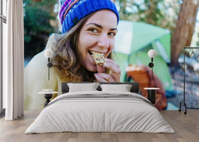 Smiling woman tourist eating snack and camping in the wild Wall mural