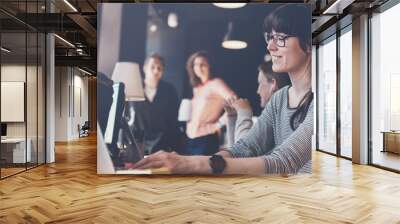 Young woman with laptop at workplace. Group of young business people working together. Big open space office. Four persons. Intentional lens flares. Wide screen, panoramic Wall mural