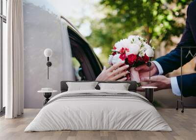 Groom gives a bouquet o=f flowers to bride who seats in a car Wall mural