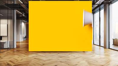 Hand holds a megaphone from a hole in the wall on a yellow background. Concept of hiring, advertising something. Banner Wall mural