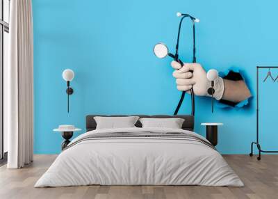 Man's hand in a medical glove holds a stethoscope on a bright blue background Wall mural