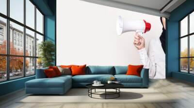 Muslim young woman with a surprised face in a hijab holds a megaphone in her hands on a light background. Banner. Looks at the camera Wall mural