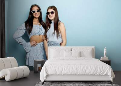 Photo of two young caucasian women in bright blue clothes standing on blue background. Brunette in sunglasses are smiling broadly with their teeth.  Wall mural