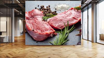 Raw beef meat and spices. Two slices of fresh raw meat, rosemary and fresh herbs on a black slate stone plate. Preparing and marinating barbecue meat. Wall mural