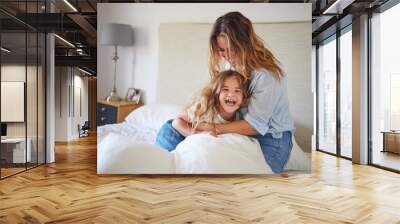 Mom and child on the bed playing together, having fun and laughing. Portrait of mother and daughter in bedroom, smiling while woman tickle young girl. Family, love and laughter in morning at home Wall mural