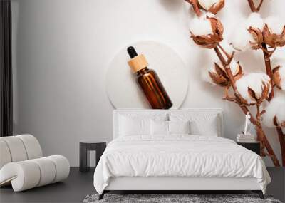 Amber glass dropper bottle with bamboo lid and cotton flowers on white concrete podium. Skincare cosmetic. Beauty concept for face body care. Presentation with daylight. Wall mural