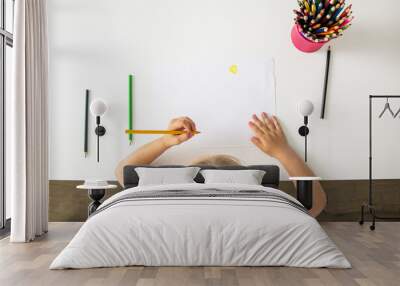 The girl draws with colored pencils sitting at a white table. Top view, flat lay Wall mural