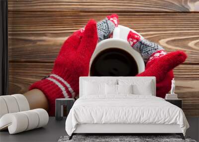 The panorama of  two hands into the red  knitted gloves holding the cup of coffee on the wooden background. Concept of winter holidays and coziness. Wall mural