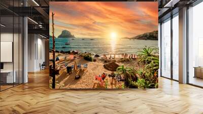 Picturesque view of Cala d'Hort tropical Beach, people hangout in beautiful beach with Es Vedra rock view during magnificent vibrant sunset glowing sun. Balearic Islands, Spain, Espana. Ibiza Wall mural