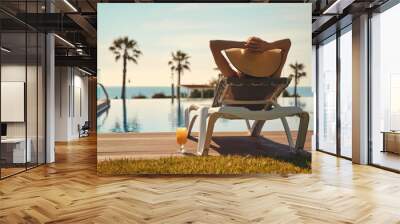 Rear view woman wear hat sunbathing on deckchair on poolside Wall mural