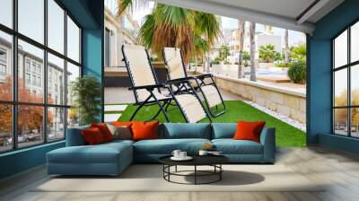 Two empty lounge chairs on artificial lawn grass inside of personal area backyard residential summer villa, view to modern homes with swimming pool, luxury, summer holidays lifestyle concept Wall mural