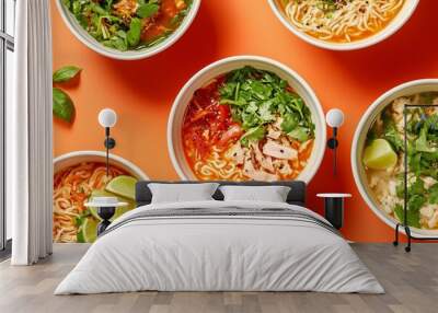 Top view of various Asian noodle bowls with fresh herbs and lime on vibrant orange background for culinary presentation. Wall mural