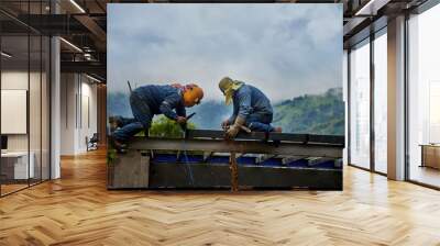 Two construction workers welding steel beams on a building structure, with a mountainous landscape in the background. Concept of teamwork, hard labor, and construction in challenging environments Wall mural